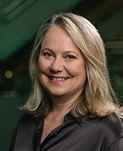 Headshot of Margaret Tregurtha. She is smiling and has short, blonde hair. She wears a black jacket and pink top